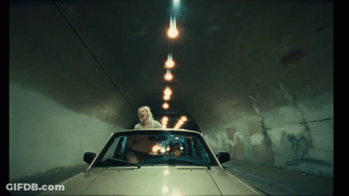 A Woman In A Car Is Driving Through A Tunnel With Lights Coming Out Of The Ceiling GIF
