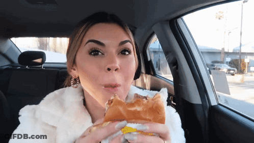A Woman In A Car Is Eating A Sandwich With Her Mouth Open GIF