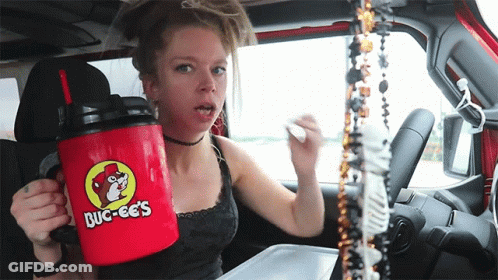 A Woman In A Car Is Holding A Red Mug That Says Buc-Ees On It GIF
