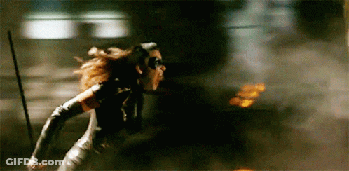 A Woman In A Catwoman Costume Is Running Through A Dark Room . GIF