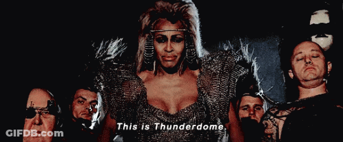 A Woman In A Chain Mail Dress Is Surrounded By Men And Says This Is Thunderdome GIF