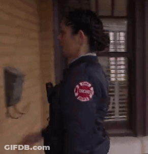 A Woman In A Chicago Fire Department Jacket Is Standing In Front Of A Window GIF