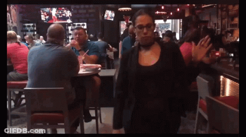 A Woman In A Choker Is Walking In A Crowded Restaurant GIF