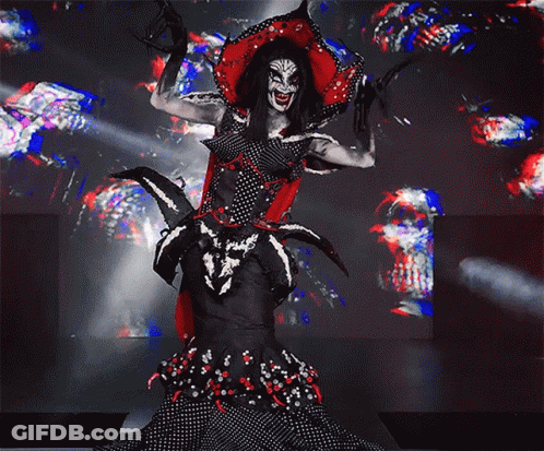 A Woman In A Clown Costume Is Standing On A Stage With Her Arms Outstretched GIF