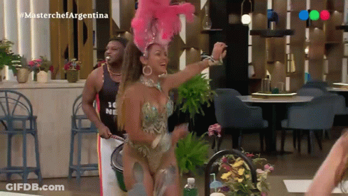 A Woman In A Colorful Costume Is Dancing In Front Of A Man Wearing A Shirt That Says Masterchef Argentina .. GIF