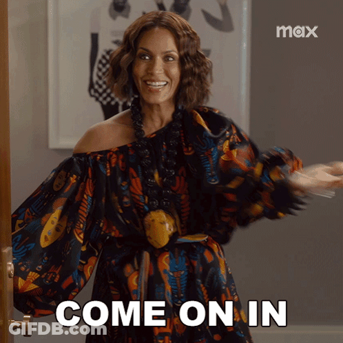 A Woman In A Colorful Dress Is Standing In Front Of A Door And Says Come On In GIF