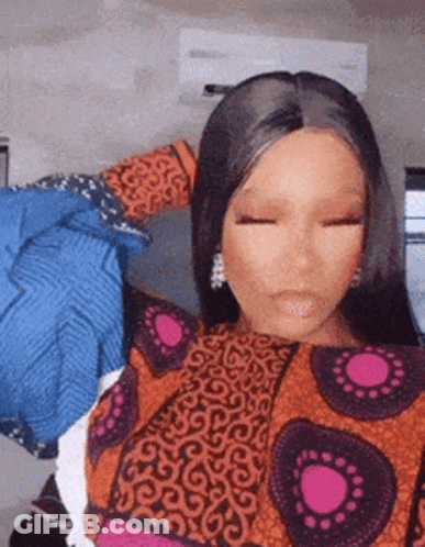 A Woman In A Colorful Dress Is Standing In Front Of A Wall With Clothes On It . GIF