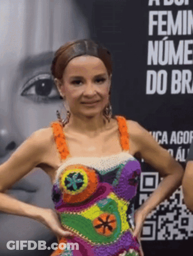 A Woman In A Colorful Dress Stands In Front Of A Sign That Says Feminin Nume Do Br GIF