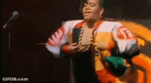 A Woman In A Colorful Jacket Is Standing In Front Of A Microphone . GIF
