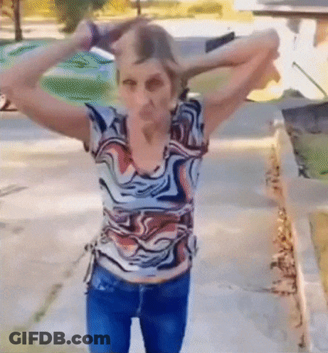A Woman In A Colorful Shirt Is Standing On A Sidewalk With Her Hands In Her Hair . GIF