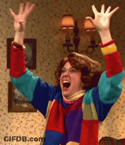 A Woman In A Colorful Sweater Has Her Arms In The Air GIF