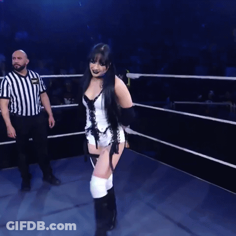 A Woman In A Corset Is Walking In A Ring With A Referee GIF