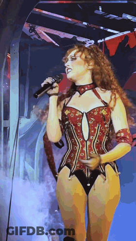 A Woman In A Corset Singing Into A Microphone On Stage GIF