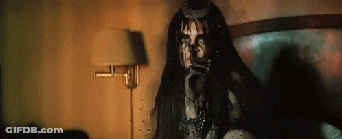 A Woman In A Costume Is Sitting On A Bed In A Room With A Lamp . GIF