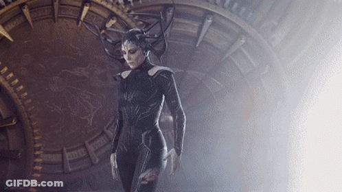 A Woman In A Costume With Horns Is Standing In Front Of A Clock That Says ' X ' On It GIF