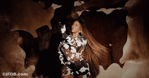 A Woman In A Cow Print Dress Is Standing In Front Of A Cow Skin Rug . GIF