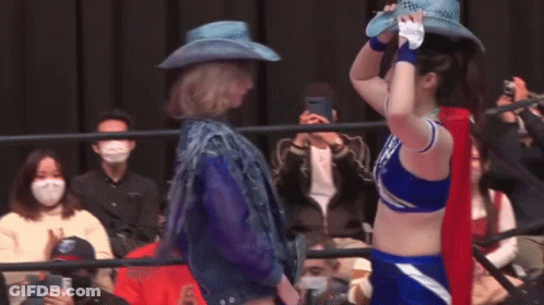 A Woman In A Cowboy Hat Is Standing Next To Another Woman In A Blue Outfit . GIF
