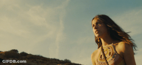 A Woman In A Crocheted Top Stands In Front Of A Cloudy Sky GIF