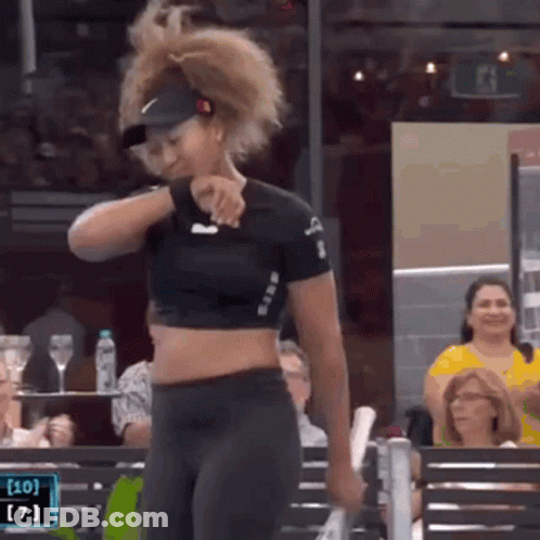 A Woman In A Crop Top And Hat Is Standing In Front Of A Crowd . GIF