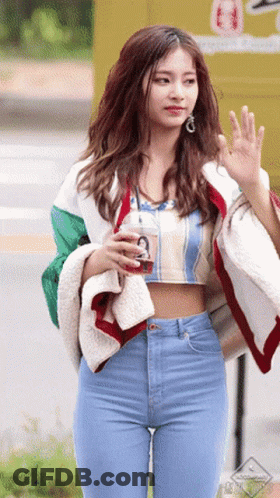 A Woman In A Crop Top And Jeans Is Holding A Drink GIF