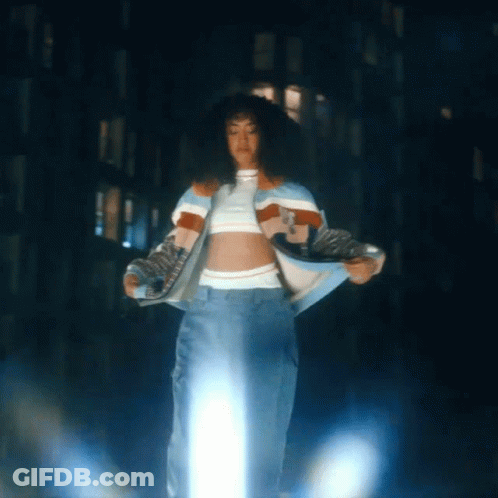 A Woman In A Crop Top And Jeans Is Standing In Front Of A Building GIF