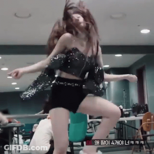 A Woman In A Crop Top And Shorts Is Dancing In A Room With A Sign That Says Vm GIF
