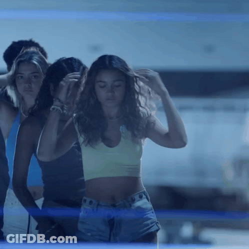 A Woman In A Crop Top And Shorts Stands In Front Of A Group Of People GIF