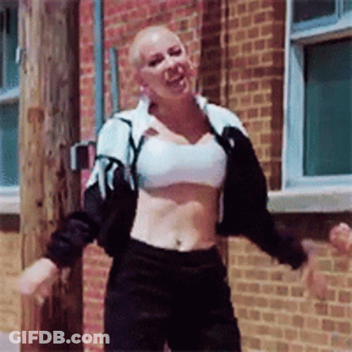 A Woman In A Crop Top Is Dancing In Front Of A Brick Wall GIF