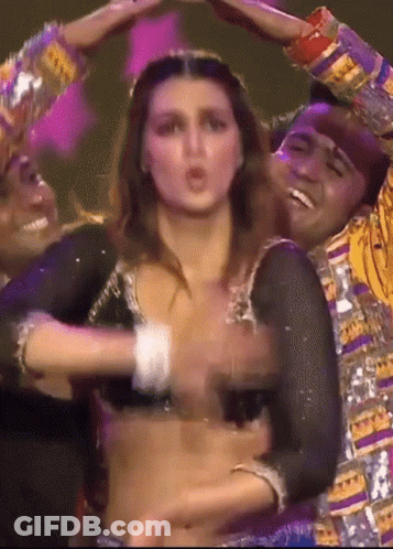 A Woman In A Crop Top Is Dancing With A Man In A Colorful Outfit . GIF