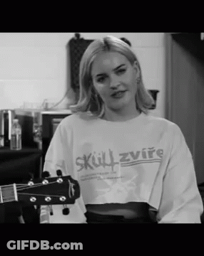 A Woman In A Crop Top Is Holding A Guitar . GIF