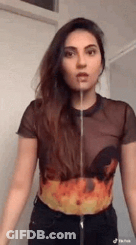 A Woman In A Crop Top With Flames On It Is Standing In Front Of A Door With Her Mouth Open . GIF