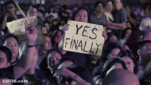 A Woman In A Crowd Holds Up A Sign That Says " Yes Finally " GIF
