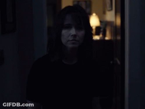 A Woman In A Dark Room With A Lamp In The Background GIF