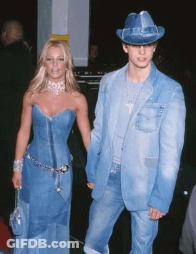A Woman In A Denim Dress Holds Hands With A Man In A Denim Suit And Hat GIF