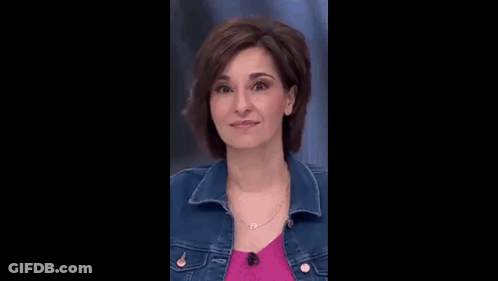A Woman In A Denim Jacket And A Pink Shirt Is Smiling . GIF