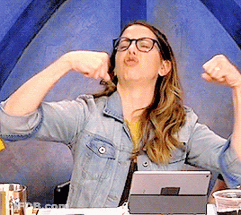 A Woman In A Denim Jacket And Glasses Is Flexing Her Muscles In Front Of A Tablet GIF