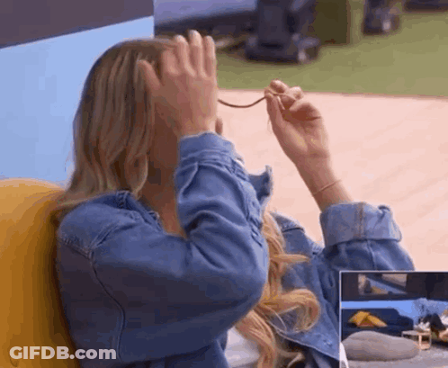 A Woman In A Denim Jacket Is Covering Her Face With Her Hands While Holding A Pair Of Glasses . GIF