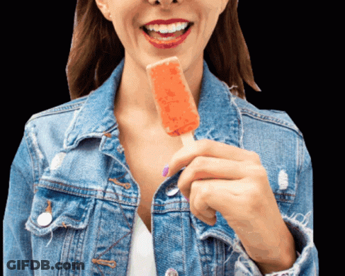 A Woman In A Denim Jacket Is Holding An Orange Popsicle GIF