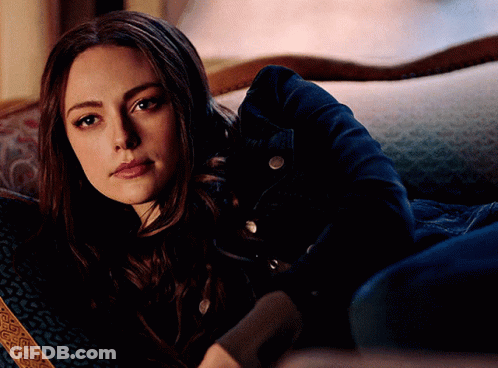 A Woman In A Denim Jacket Is Laying On A Couch Looking At The Camera GIF