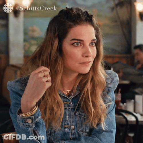 Woman In Denim Jacket Sitting At Table With Schitts Creek Logo GIF