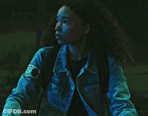 A Woman In A Denim Jacket Is Standing In The Dark . GIF
