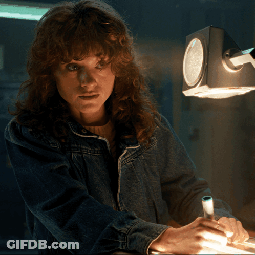 A Woman In A Denim Jacket Is Writing On A Piece Of Paper Under A Clock GIF