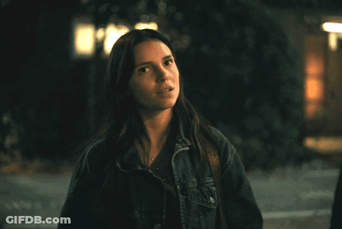 A Woman In A Denim Jacket Stands In Front Of A Building At Night GIF