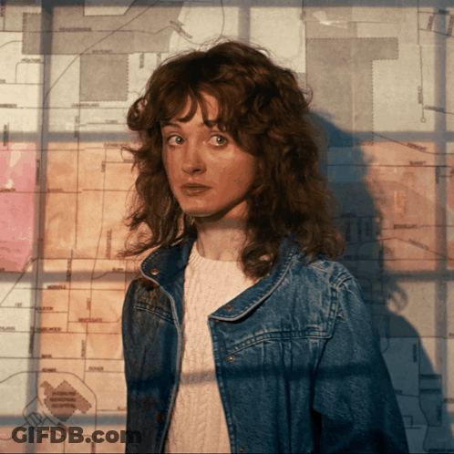 A Woman In A Denim Jacket Stands In Front Of A Map That Says The T On It GIF