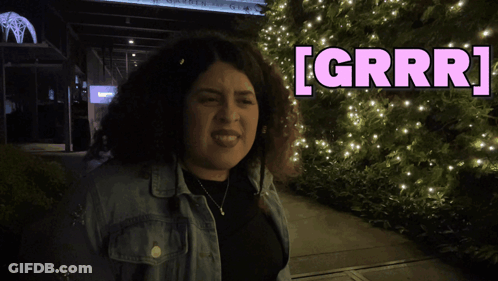 A Woman In A Denim Jacket Stands In Front Of A Sign That Says Grrr GIF