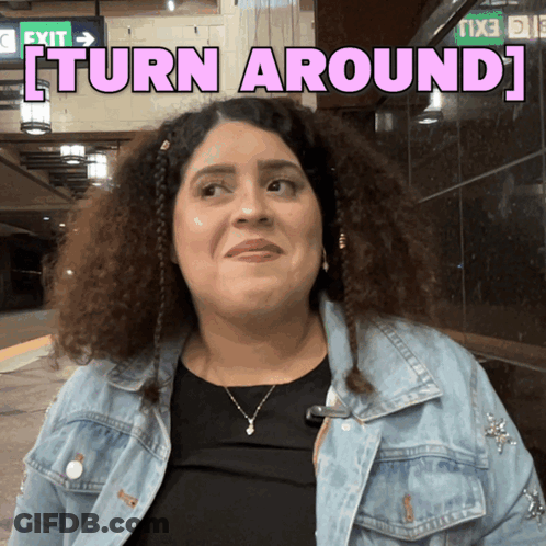 A Woman In A Denim Jacket With The Words Turn Around Behind Her GIF