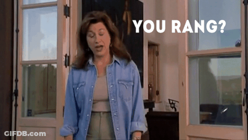 A Woman In A Denim Shirt Is Standing In Front Of A Door With The Words " You Rang " On The Bottom GIF