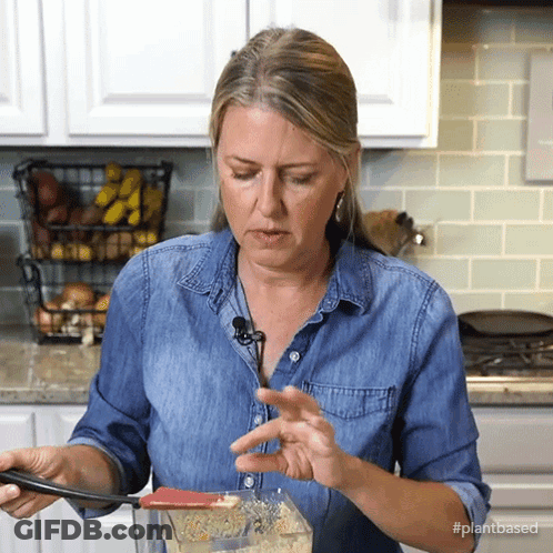 A Woman In A Denim Shirt Is Stirring Something In A Blender With The Hashtag #Plantbased On The Bottom GIF