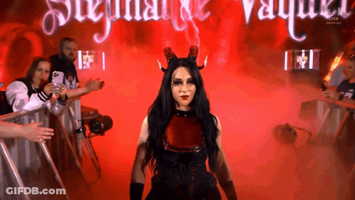 A Woman In A Devil Costume Stands In Front Of A Sign That Says ' Stephanie Vaughn ' GIF
