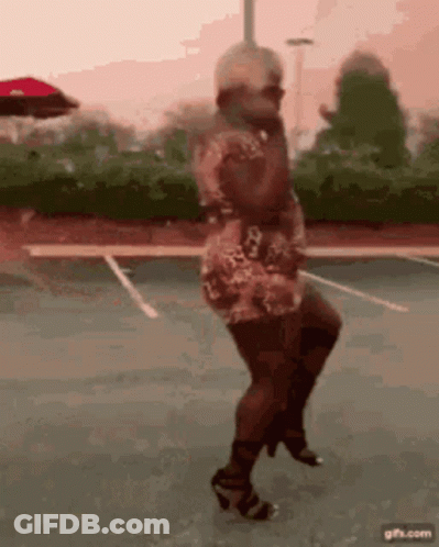 A Woman In A Dress And Heels Is Dancing On A Parking Lot . GIF